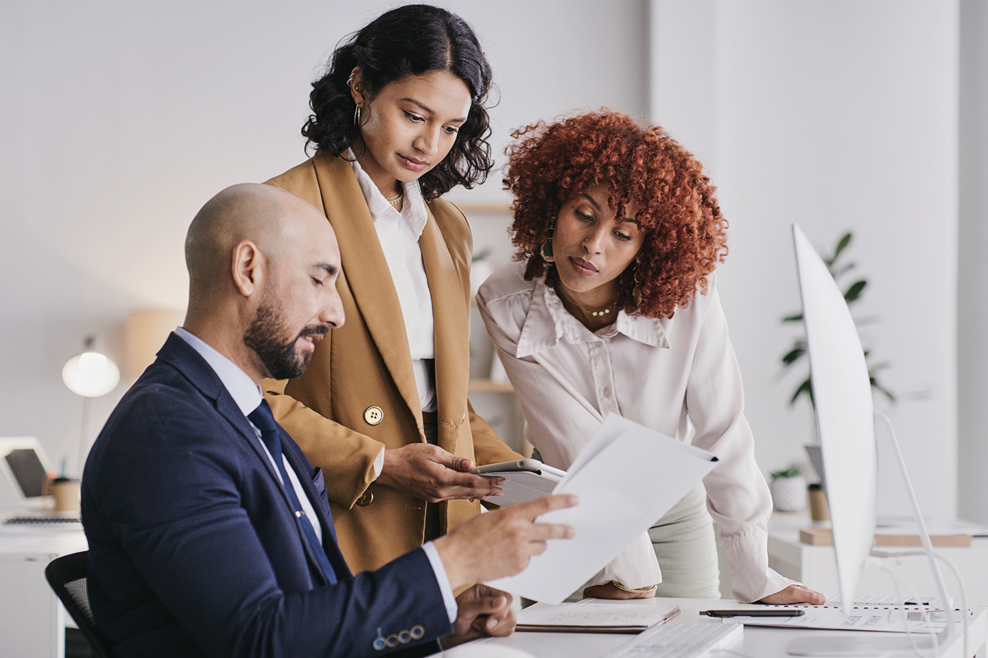 Three professionals in an office comparing notes; a man and two women