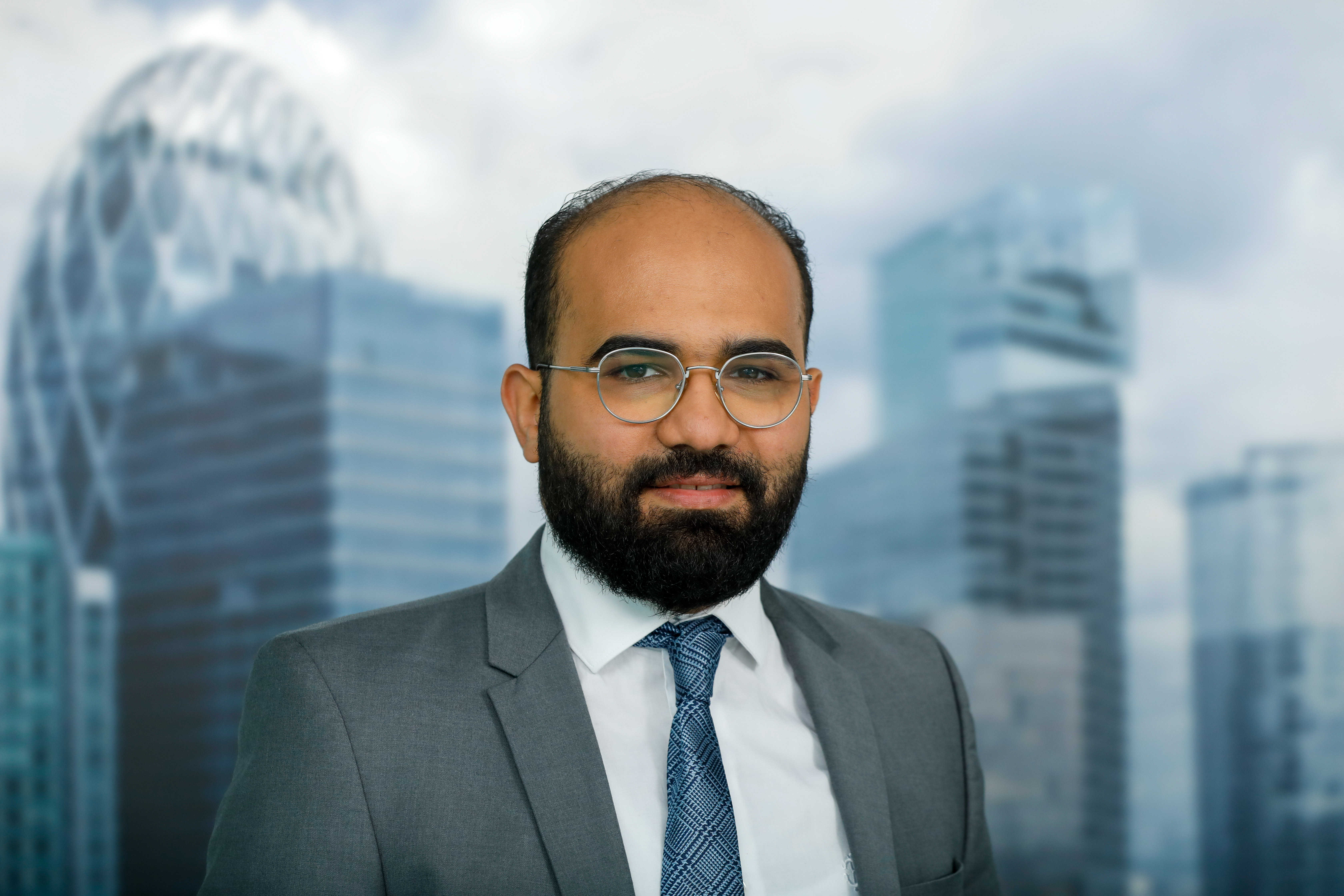 Professional headshot of a man in a suit with a cityscape in the background